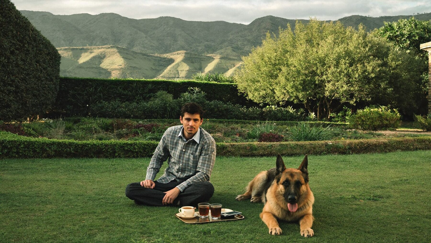 A man on a lawn in Islamabad with a german shepherd resting beside him