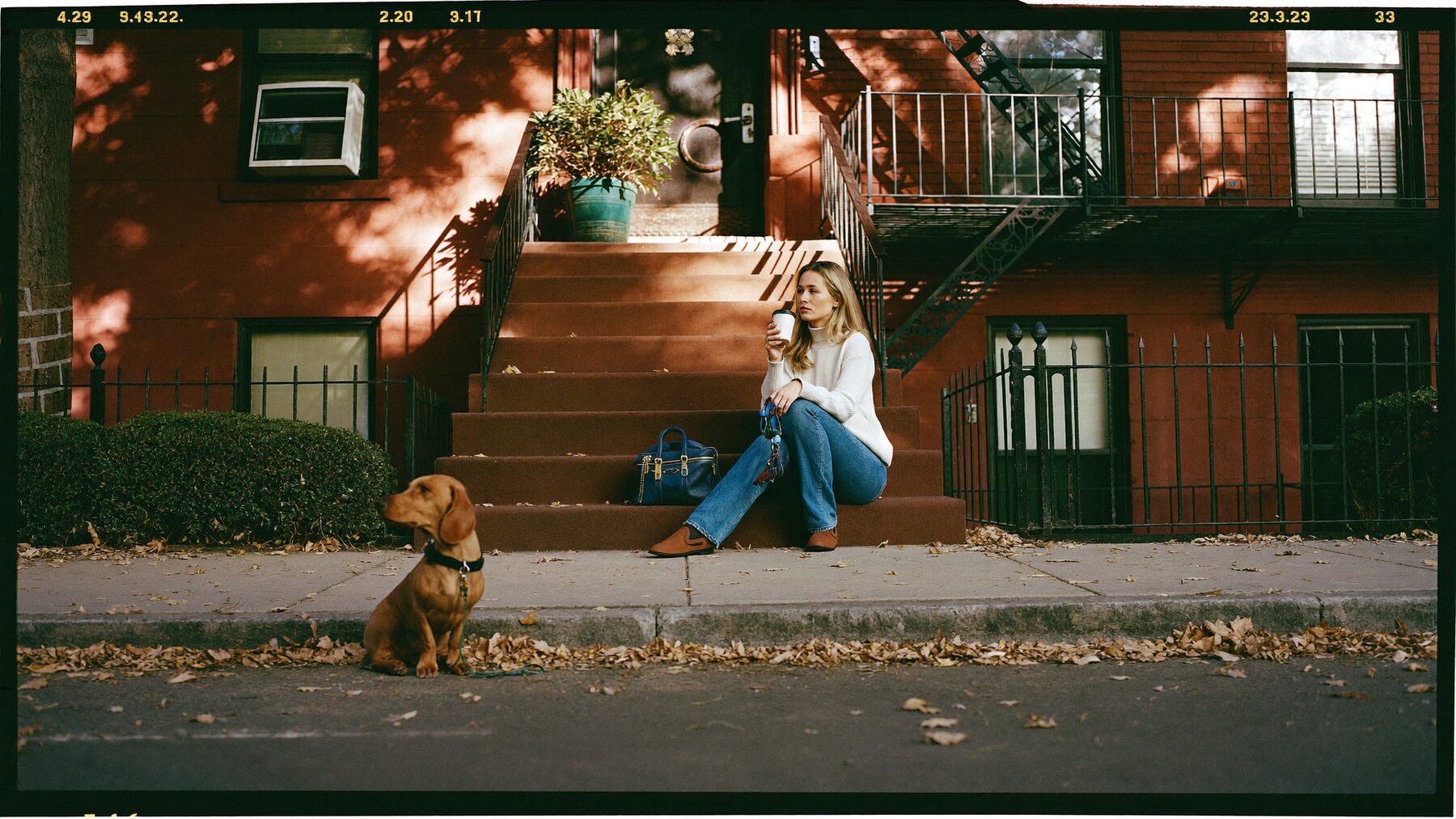 A dachshund on a Brooklyn brownstone stoop beside a woman with keys and a coffee